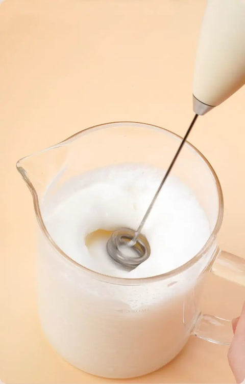 Top Tier Handheld Milk Frother Packs Serious Oomph For Crafting Silky Foam On The Fly in a glass pitcher.