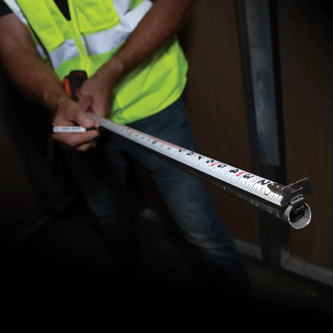 Person using Heavy-Duty Tape Measure With Nylon-Coated Blade, 25-Foot Reach, Double-Hook, Double-Sided Measurements in dim setting