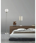 Fiona Torchiere Floor Lamp In Brushed Steel With Marble Base And Opal Glass Shade beside bed in modern bedroom.