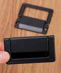 Close-up of a foldable black zinc alloy drawer pull, highlighting space-saving design. 2 Pack Foldable Zinc Alloy Drawer Pulls For Cabinets And Furniture Hidden Metal Handles In Black Space Saving Durable And Corrosion Resistant 7.4 By 4 Cm Easy Install.