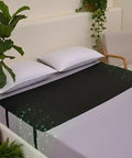 Black bedside grounding mat for sleep and deep relaxation on a bed with no electricity needed, plants in background