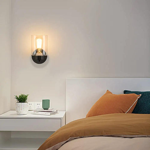 One Light Matte Black Bathroom Vanity Sconce With Clear Glass Shade Vintage Style Wall Light Fixture beside a bed