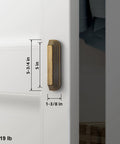 Side view of installed 5-inch antique brass cup pull with distinctive layered ribbed multi-sectioned design on white cabinet.