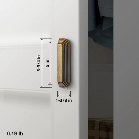 Side view of installed 5-inch antique brass cup pull with distinctive layered ribbed multi-sectioned design on white cabinet.