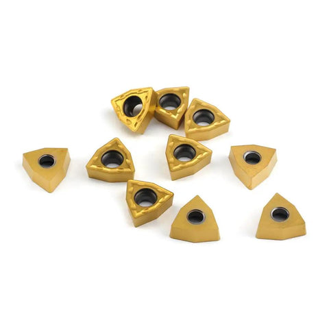 10 gold-colored Pro Grade Carbide Turning Inserts WCMT06T304 WCMT32.51 Diamond 55 Degree Chipbreaker scattered on white surface.