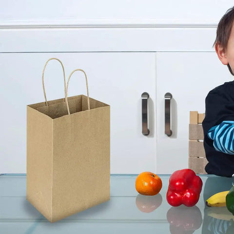 Small Natural Kraft Paper Gift Bags With Handles 5.25x3.25x8.25 Inch shown on a table with fruits, ideal for parties and crafts.