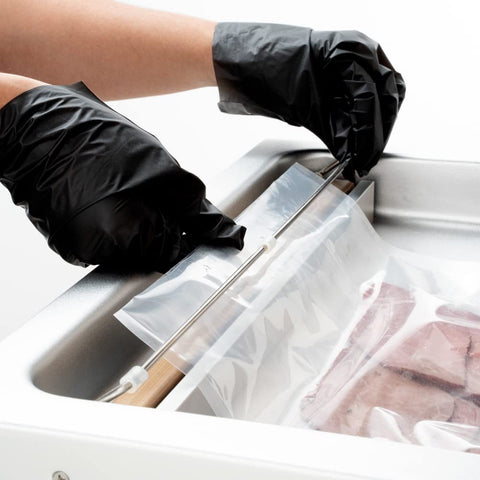 Hands in black gloves sealing a bag with a Pro Grade Chamber Vacuum Sealer Packs A Solid Punch With Sturdy 16 Inch Seal Bar And Whisper Quiet Motor.