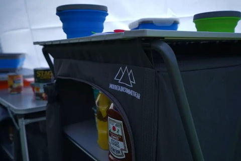 Close-up of Foldable Roll Top Camping Pantry And Table With Sturdy Aluminum Frame Durable 600 Denier Oxford Fabric set up with items.