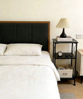 3-Tier Black Storage Shelf With Industrial X-Frame Design beside bed in bedroom holding books and clock