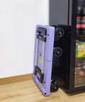 Heavy Duty Folding Trolley Cart With Slick Nylon Rollers And Sturdy Aluminum Frame telescoping grip, folded next to a fridge.