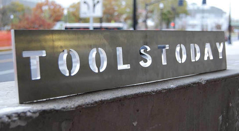 A metal sign with 'TOOLSTODAY' cut out, displayed outdoors; CNC machining example.