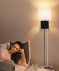 Woman reading in bed next to a Plug In Wall Sconce With USB Charging Port And Dimmable Switch, black finish, bedroom setting