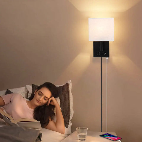 Woman reading in bed next to a Plug In Wall Sconce With USB Charging Port And Dimmable Switch, black finish, bedroom setting