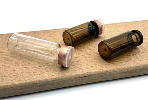 Front view: GISUREM 10ml glass vials, one clear and two amber borosilicate with pink flip-off caps on a wooden surface.