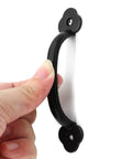 Close-up of a hand holding a black metal handle from the 12 Pack Rustic Barn Door Handles Set 4 Inch Length Hole To Hole 3.2 Inches.