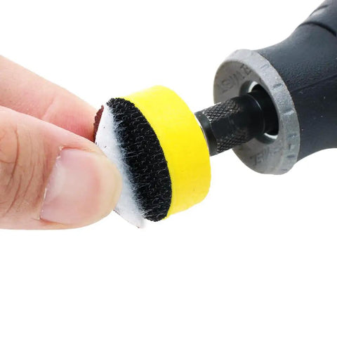 Close-up of a hand holding a 1-inch sanding disc with hook and loop backing attached to a mandrel from the 110 Piece 1 Inch Sanding Discs Set With 2 Mandrels And Hook And Loop Shank Pads 40 To 600 Grit Polishing Kit For Rotary Tool Or Drill Use On Wood Metal And Plastic.