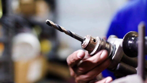 Drill bit in a drill chuck held by a hand, close-up view with a blurred workshop background