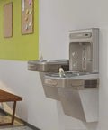 EZH2O Bottle Filling Station With Bi Level ADA Cooler Filtered Non Refrigerated Stainless Steel Hydration Station Featuring Touchless Sensor Sleek 1.5 GPM Fill Rate And LED Filter Status Indicator mounted on a wall.