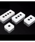 Four white plastic button box enclosures with gray bases; top panels have three circular knockouts