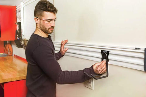 A man installs a VersaTrack Garage Storage Rail With Twenty Piece Mounting Accessories For Drywall Studs And Masonry on a garage wall.