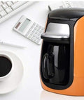 Compact Automatic Bean To Cup Coffee Maker With Heavy Duty Reusable Filter For Espresso Cappuccino And Hot Cocoa Quick Smooth Drip Brewer on a desk next to a cup of coffee.