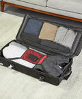 Amazon Basics 35-inch black rolling duffel bag opened to reveal packed clothes and interior pockets.