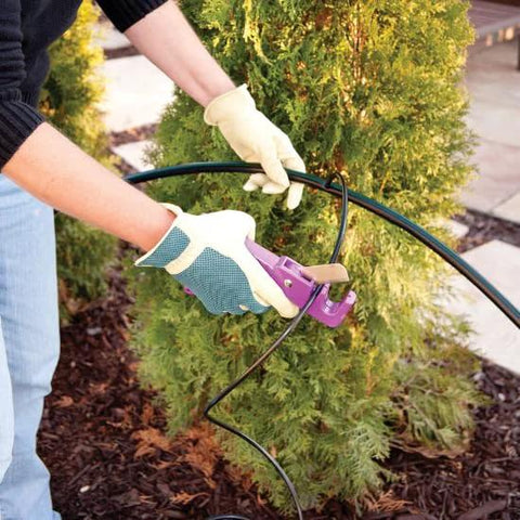 Drip irrigation tubing, 1/4-inch black, installed outdoors with gloved hands using a purple tool.