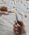 Hands holding tools with Round Wooden Smile Face Beads Set, 50 Pieces Doll Head Wood Beads, Loose Beads for DIY jewelry.