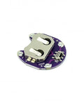 Circular purple PCB close-up with metal coin-cell battery holder, slider switch, and 6-pin header.