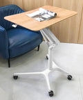 Hella Stable Mobile Standing Desk Featuring Instant Gas Spring Lift And Smooth Glide Rollers For A Total Game Changer Home Office Upgrade Or Flexible Workspace Setup In Clean Black next to a blue chair.