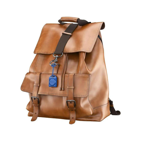 AirTag Holder Case With Key Ring And 3M Mount on backpack, IPX8 waterproof, discreet fit, blue, attached to brown leather bag.