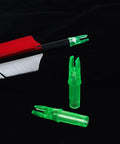 Green Press-In Arrow Nocks For Carbon Arrows.244/.246 Throat, 50 Pack Plastic Nocks next to arrow, black background