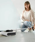 Woman using Cordless Electric Floor Sweeper Broom With Whisper Quiet Rollers For Hardwood Vinyl Tile And Rugs in a modern home.