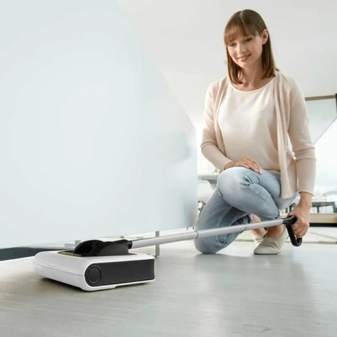 Woman using Cordless Electric Floor Sweeper Broom With Whisper Quiet Rollers For Hardwood Vinyl Tile And Rugs in a modern home.