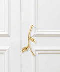 Gold ergonomic metal cabinet handle mounted on white cabinet, depicting ergonomic metal cabinet handles and drawer pulls for cabinets.