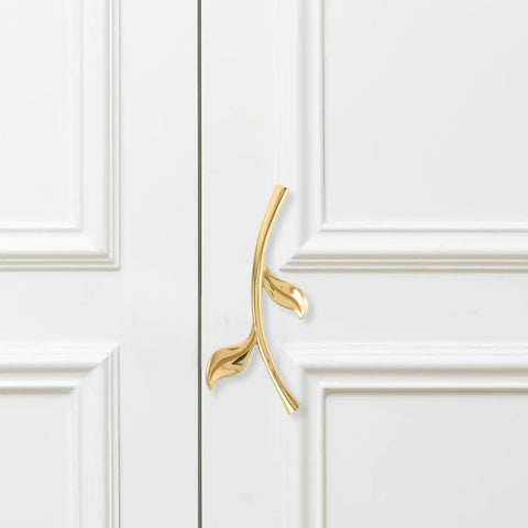 Gold ergonomic metal cabinet handle mounted on white cabinet, depicting ergonomic metal cabinet handles and drawer pulls for cabinets.