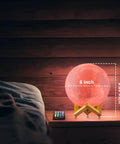 Lit Moon Lamp 3D Printed LED Night Light With 16 Color RGB Modes Remote And Touch Control Adjustable Brightness USB Recharge Realistic 6 Inch Moon Decor For Kids And Birthday Gift. Shown lit on a bedside table with remote control.