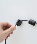 Hand using D Wings Cord Clips Nail Free Cable Organizer Kit Black Assorted Size to hold cable on wall.