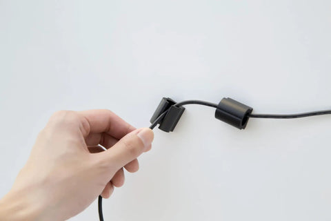Hand using D Wings Cord Clips Nail Free Cable Organizer Kit Black Assorted Size to hold cable on wall.