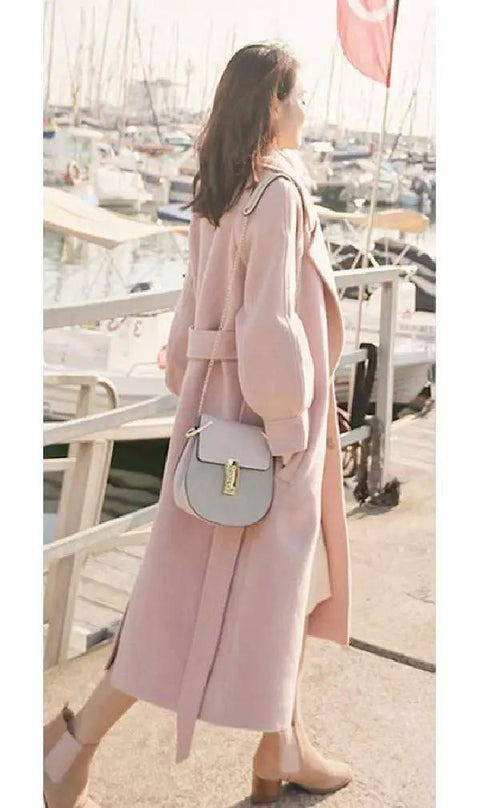 Woman wearing a pink oversized coat and carrying a grey handbag by the marina, perfect for casual spring outings.