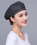 Custom Logo Chef Beret And Barista Hat For Kitchen Crew Offering Breathable Embroidered Name Cook Skullcap In Sleek Black Slick Go To Food Service Gear worn by model, profile view.