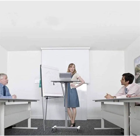 Hella Sturdy Height Adjustable Mobile Standing Desk With Smooth Glide Casters And Rustproof White Steel Top Portable Laptop Workstation And Rolling Podium For Home Office Space in a meeting room with presenters and attendees.