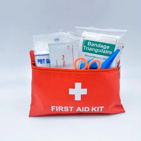Red compact travel first aid kit pouch with white cross; visible contents include bandages, scissors, prep pad.