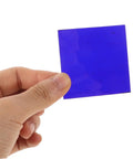 Hand holding a cobalt glass sheet 5x5cm for chemistry flame color reaction tests, heat resistant lab plate, blue color.