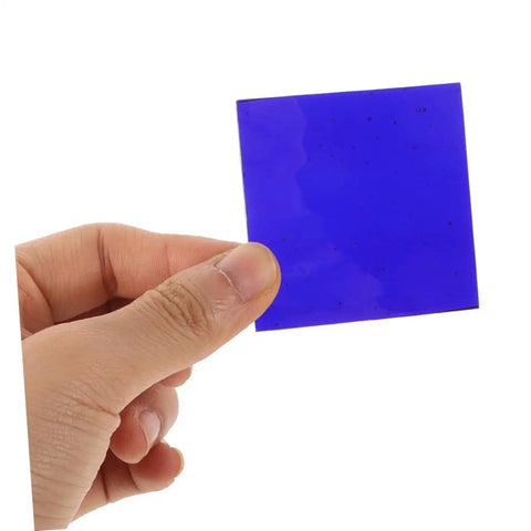 Hand holding a cobalt glass sheet 5x5cm for chemistry flame color reaction tests, heat resistant lab plate, blue color.