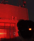 Person using Red LED Hunting Headlamp With Rechargeable Battery, illuminating building façade with red light during night hunting.