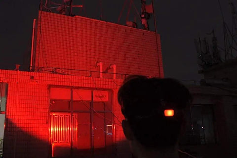Person using Red LED Hunting Headlamp With Rechargeable Battery, illuminating building façade with red light during night hunting.