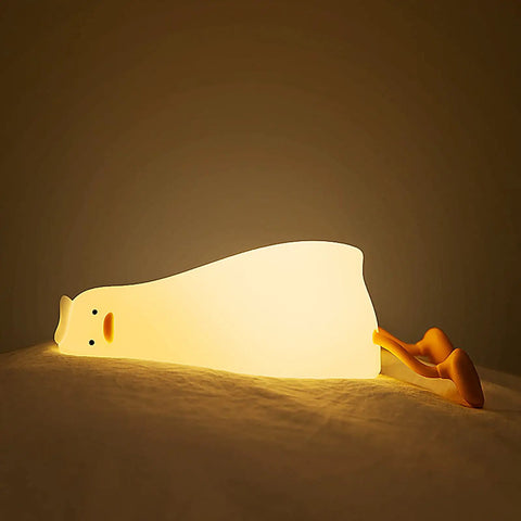 Flat Lying Duck Night Light For Kids Soft Silicone Nursery Lamp glowing with cozy warm light on a bed, showcasing its adorable design.