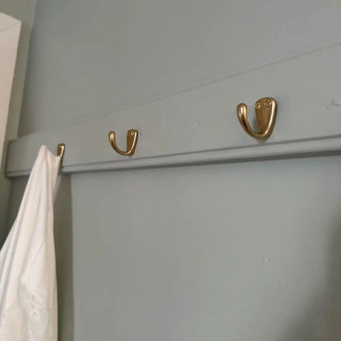 Small Solid Brass Wall Mounted Hanging Hooks Duo Pack Slick Dope Gold Finish on wall holding white clothing.