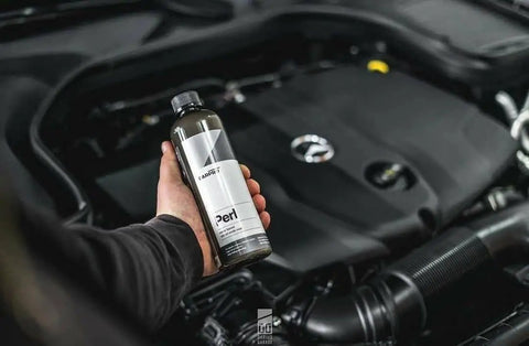 Person holding 500 mL bottle of Perl Coat Plastic And Rubber Protectant For Cars near engine bay